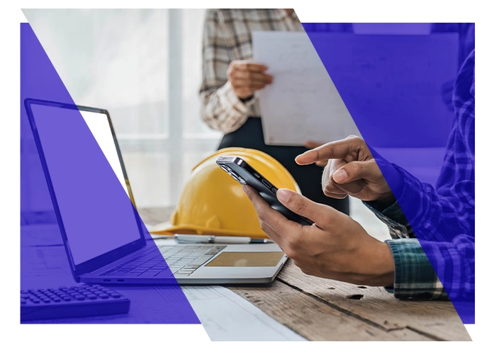 Plumbing team member using a smartphone beside a laptop and hard hat