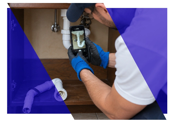 Plumbing technician photographing pipes under a sink with a smartphone