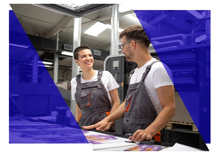 Print shop employees reviewing printed materials beside commercial printing equipment